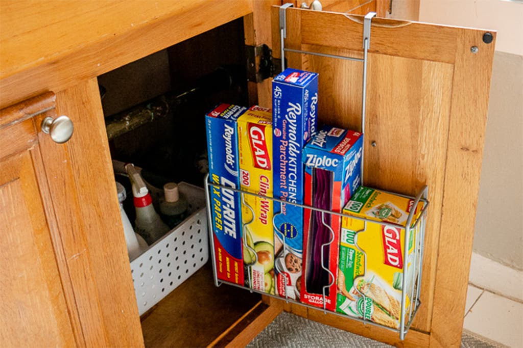 Wire rack mounted on the inside of a wooden cabinet door holding rolls of foil, plastic wrap, and storage bags.