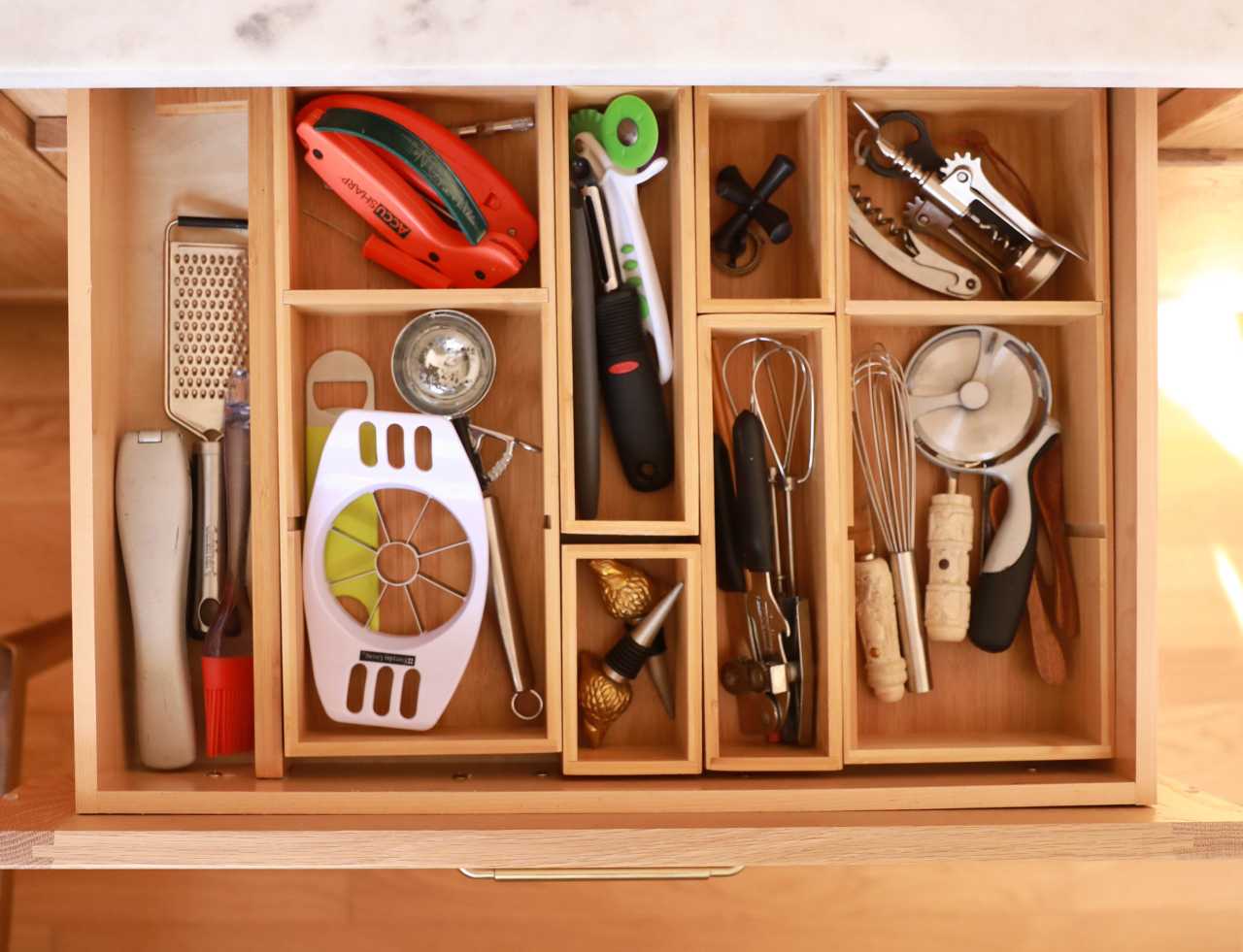 Wooden drawer insert neatly separating various kitchen tools, utensils, and gadgets.